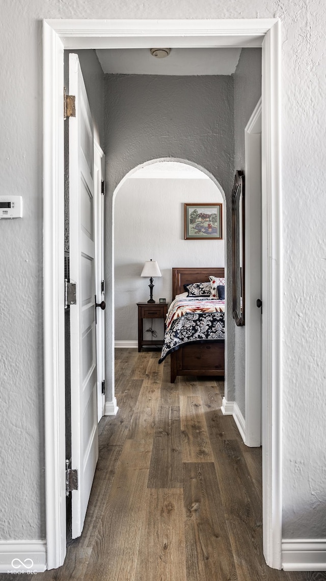 hall featuring arched walkways, a textured wall, baseboards, and wood finished floors