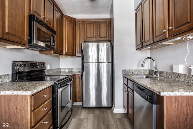 kitchen featuring baseboards, appliances with stainless steel finishes, light stone countertops, a textured ceiling, and a sink