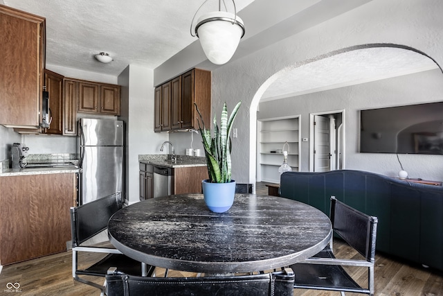 dining space with a textured ceiling, dark wood-type flooring, arched walkways, and built in shelves