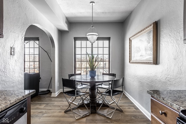 dining room featuring dark wood-type flooring, arched walkways, a textured wall, and baseboards