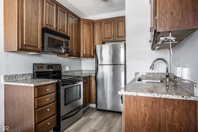 kitchen with light stone countertops, a textured ceiling, appliances with stainless steel finishes, and a sink