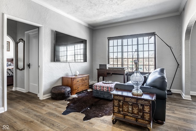 living area with ornamental molding, arched walkways, a textured wall, and wood finished floors