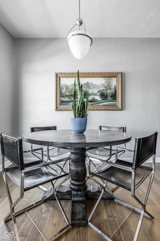 dining area featuring a textured ceiling, a textured wall, wood finished floors, and baseboards