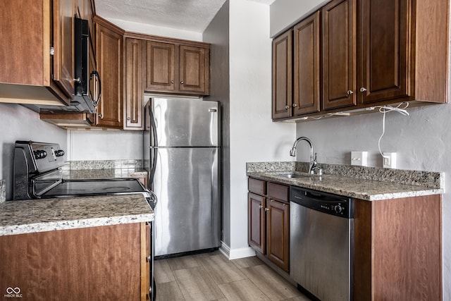 kitchen with a textured ceiling, stainless steel appliances, a sink, and baseboards