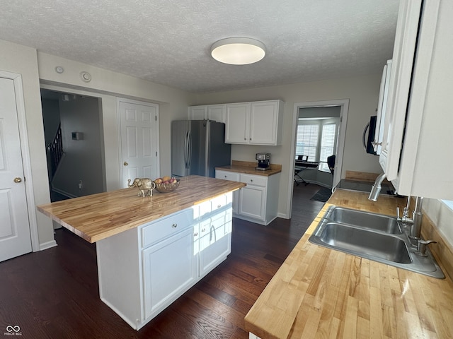 kitchen featuring sink, butcher block countertops, a center island, stainless steel refrigerator, and white cabinets