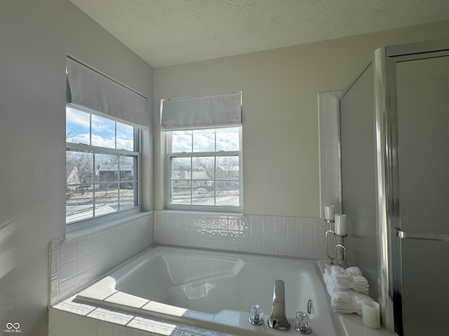 bathroom with tiled bath and a textured ceiling