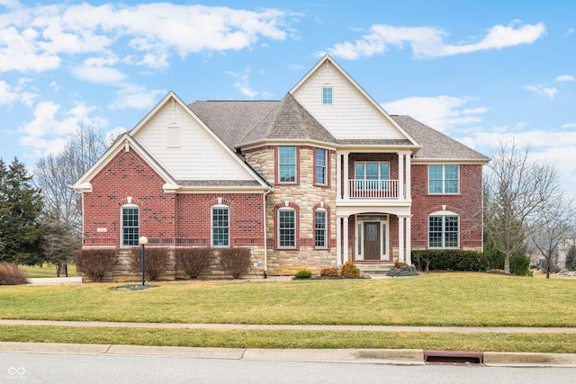 view of front of house featuring roof with shingles, brick siding, a front yard, a balcony, and stone siding