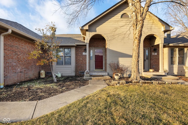 view of front of home with brick siding, a front yard, and a shingled roof