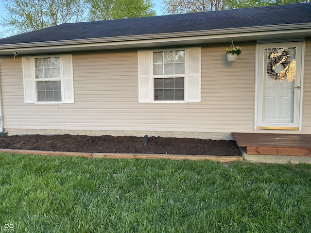 entrance to property with roof with shingles and a yard