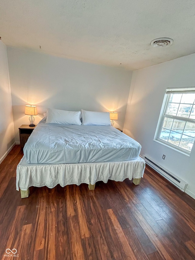 bedroom featuring a baseboard heating unit, dark wood-style floors, visible vents, and baseboards