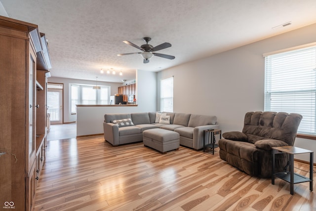 living room with light wood-type flooring, a textured ceiling, visible vents, and a wealth of natural light