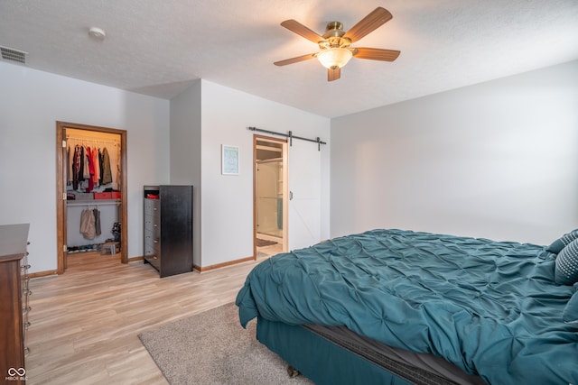 bedroom featuring light wood finished floors, a barn door, visible vents, and a textured ceiling