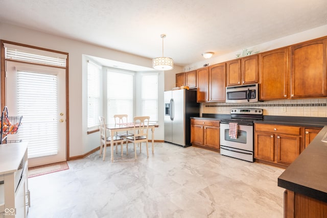 kitchen with decorative light fixtures, stainless steel appliances, dark countertops, backsplash, and brown cabinetry