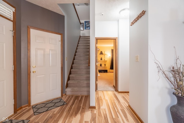 foyer with stairway, baseboards, light wood-style flooring, and a textured ceiling