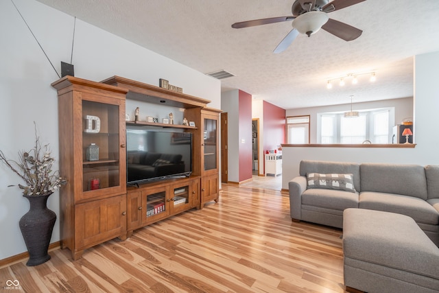 living area featuring a textured ceiling, ceiling fan, light wood-style flooring, visible vents, and baseboards