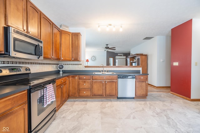 kitchen featuring stainless steel appliances, dark countertops, brown cabinets, and a sink