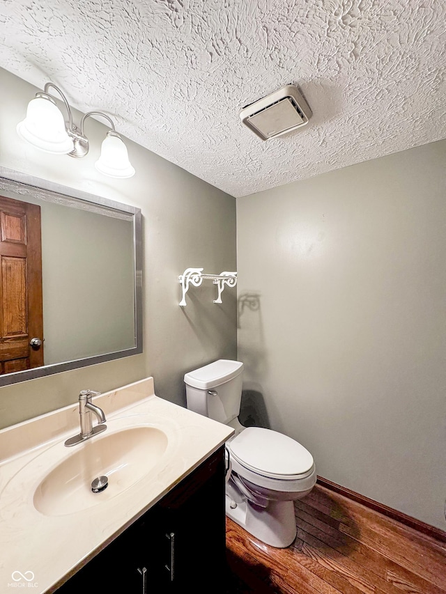 half bath with baseboards, toilet, vanity, wood finished floors, and a textured ceiling