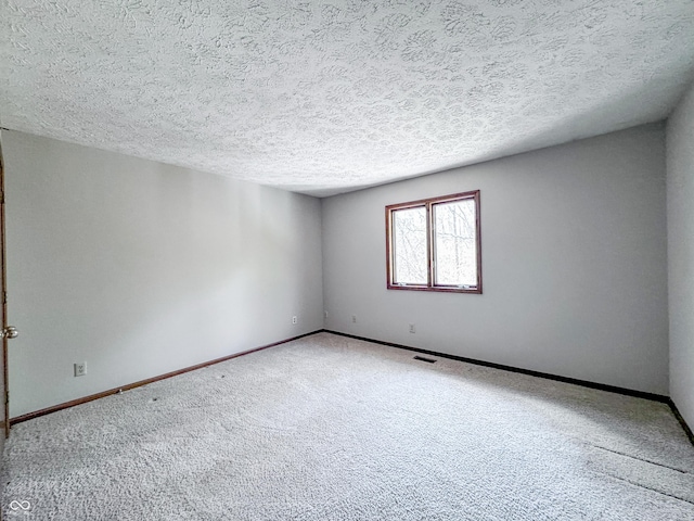 empty room featuring a textured ceiling, carpet, visible vents, and baseboards