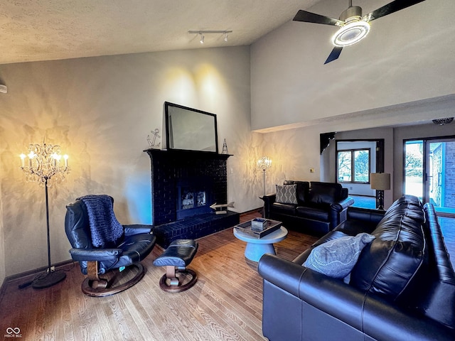 living room featuring ceiling fan with notable chandelier, a fireplace, a textured ceiling, and wood finished floors