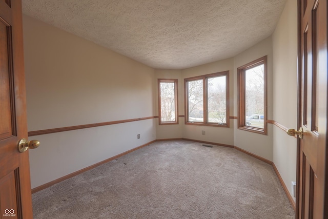 spare room with light carpet, visible vents, a textured ceiling, and baseboards