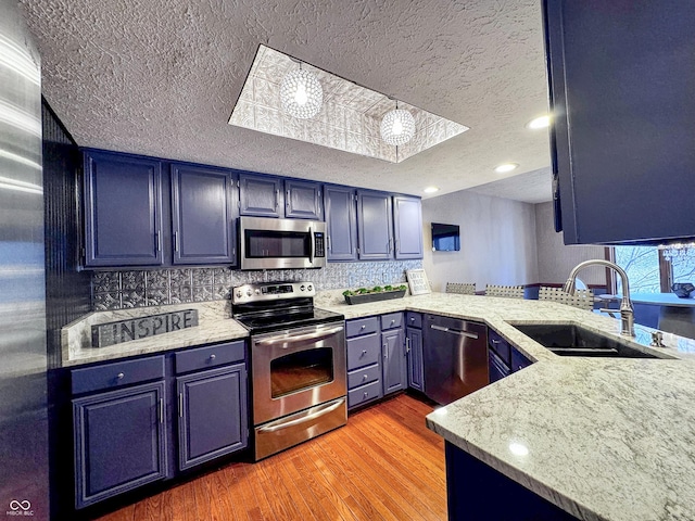 kitchen featuring tasteful backsplash, light wood-type flooring, appliances with stainless steel finishes, a textured ceiling, and a sink