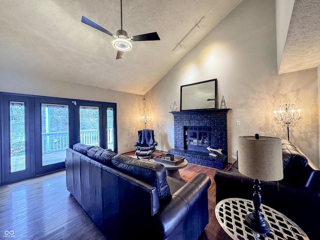 living room with a brick fireplace, lofted ceiling, ceiling fan with notable chandelier, wood finished floors, and a textured ceiling