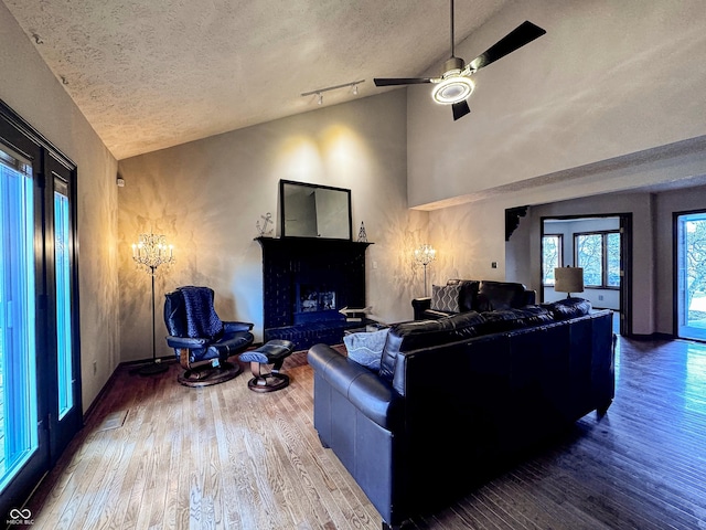 living area with track lighting, a brick fireplace, ceiling fan, wood finished floors, and a textured ceiling