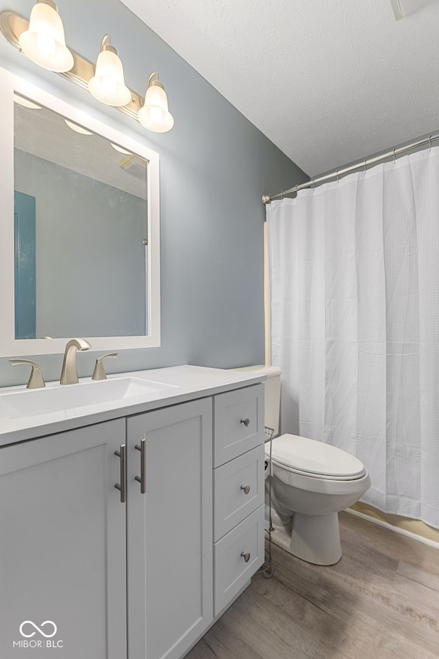 bathroom with toilet, a textured ceiling, wood finished floors, and vanity