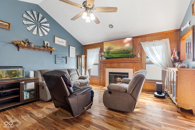 living area with ceiling fan, a tile fireplace, vaulted ceiling, and wood finished floors