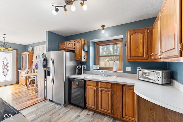 kitchen featuring pendant lighting, black dishwasher, brown cabinets, light countertops, and a sink