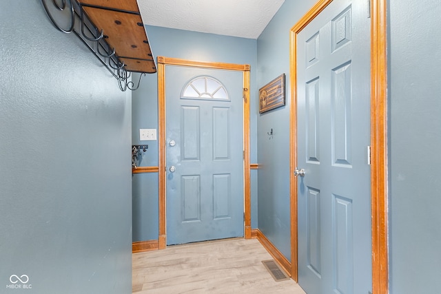 foyer featuring a textured ceiling, light wood-style flooring, visible vents, and baseboards