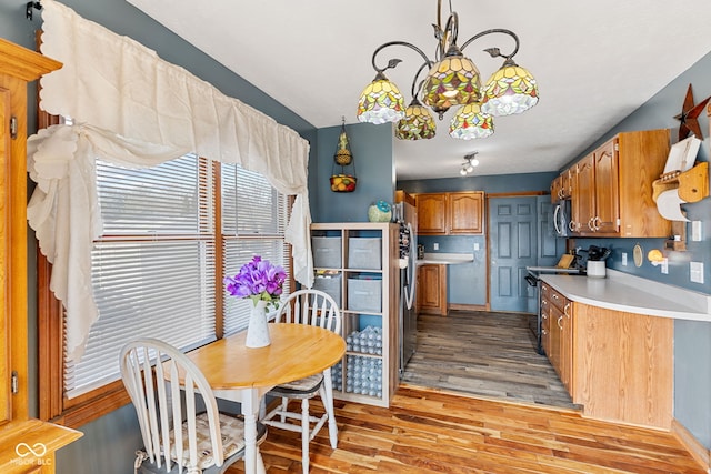 kitchen featuring light countertops, appliances with stainless steel finishes, hanging light fixtures, light wood-type flooring, and brown cabinetry