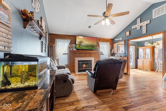 living area featuring light wood-type flooring, visible vents, vaulted ceiling, and a tiled fireplace