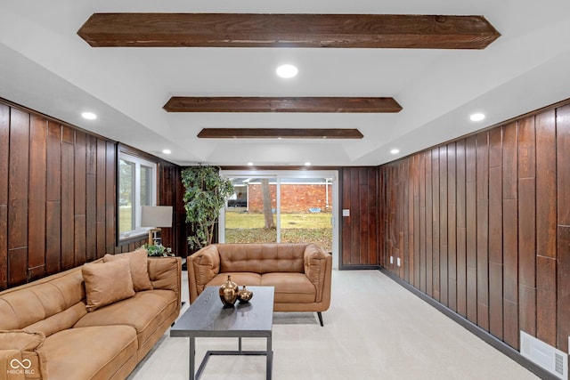 carpeted living room with beamed ceiling, plenty of natural light, and wood walls