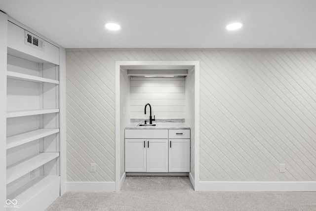 bar with white cabinetry, sink, and light carpet