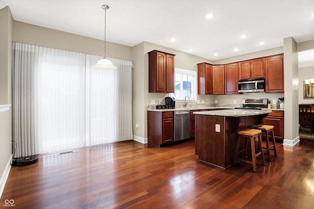 kitchen featuring a kitchen island, appliances with stainless steel finishes, pendant lighting, a kitchen bar, and dark hardwood / wood-style flooring