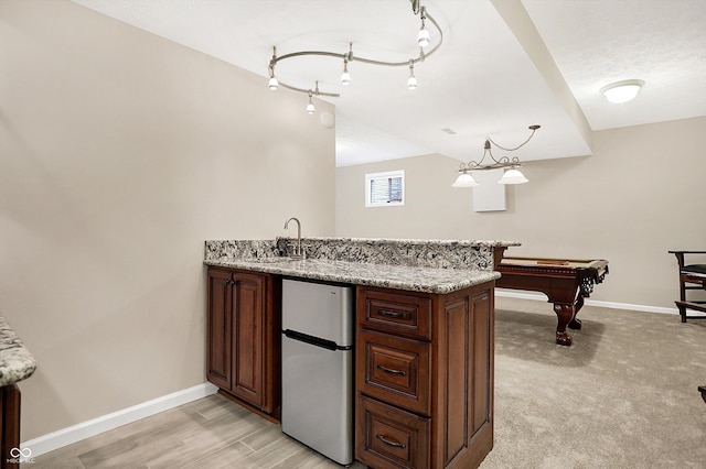 kitchen featuring sink, hanging light fixtures, light stone countertops, and stainless steel refrigerator