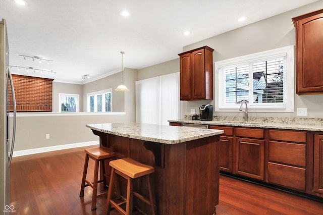 kitchen with pendant lighting, sink, dark wood-type flooring, light stone counters, and a kitchen island