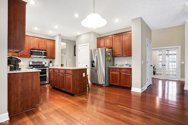 kitchen with pendant lighting, dark wood-type flooring, stainless steel appliances, light stone countertops, and a kitchen island