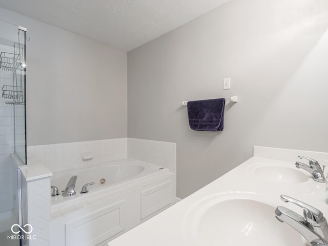 bathroom with a textured ceiling, a tub with jets, a tile shower, and a sink