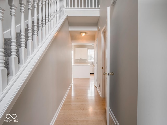 corridor featuring a towering ceiling, light wood finished floors, and baseboards