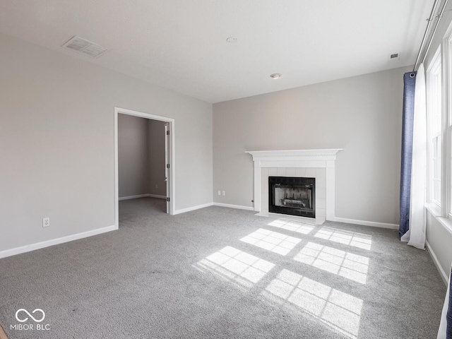 unfurnished living room featuring a wealth of natural light, baseboards, visible vents, and a tiled fireplace