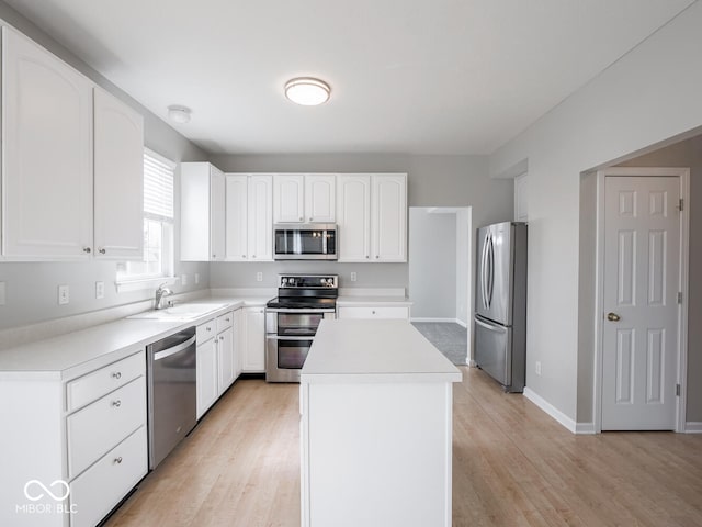 kitchen with light countertops, appliances with stainless steel finishes, white cabinets, a sink, and a kitchen island