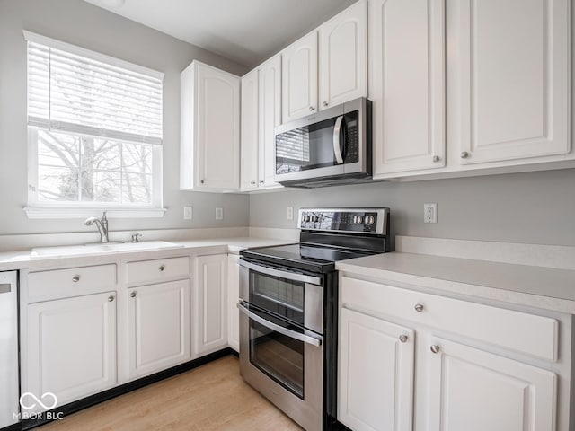 kitchen featuring light wood finished floors, white cabinets, appliances with stainless steel finishes, light countertops, and a sink