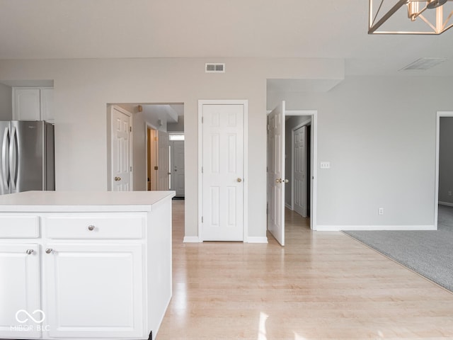 interior space featuring visible vents, baseboards, freestanding refrigerator, light countertops, and white cabinetry