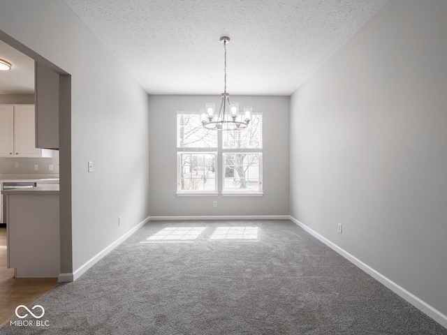 unfurnished dining area with carpet flooring, a textured ceiling, baseboards, and an inviting chandelier