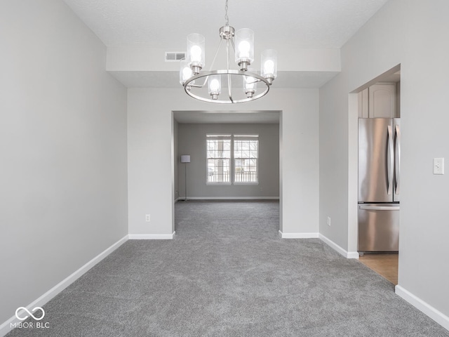 carpeted empty room with baseboards, visible vents, and a notable chandelier