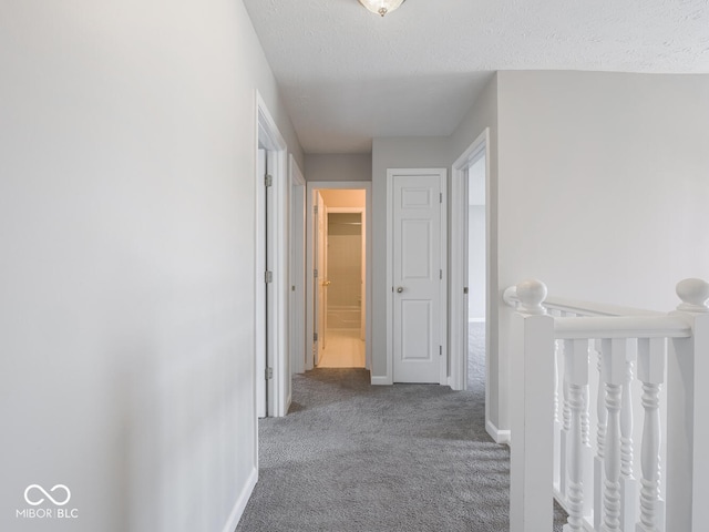 corridor featuring a textured ceiling, carpet flooring, and baseboards