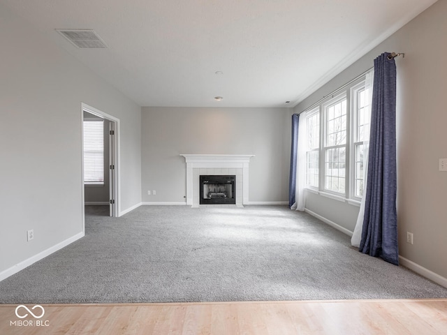 unfurnished living room featuring carpet floors, visible vents, a tiled fireplace, wood finished floors, and baseboards