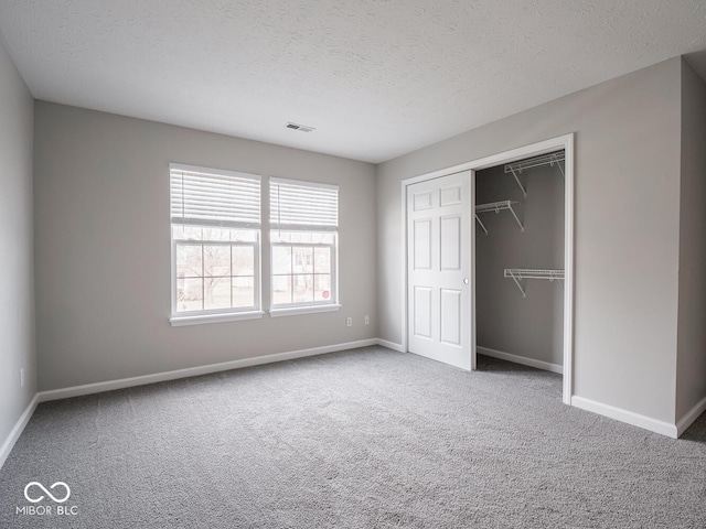 unfurnished bedroom with visible vents, baseboards, a textured ceiling, carpet floors, and a closet